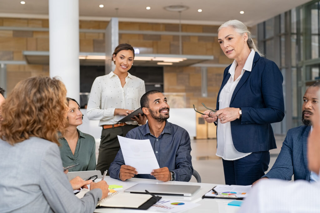 Group of mixed race business people discussing work in conference room. Senior business manager guiding employees in meeting. Group of businessman and businesswoman working together while brainstorming and sharing new ideas and strategy.