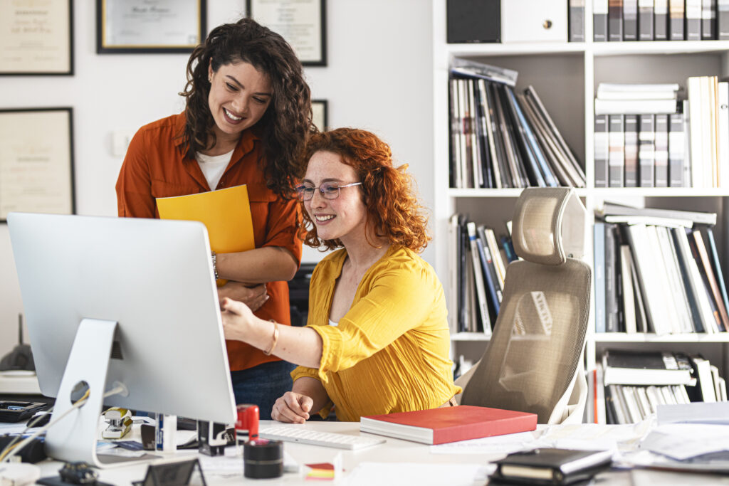 Two female coworkers trying to solve problem.of new project.They sitting at the desk and using computer.Working day at the office.